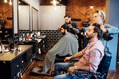 Hairdressers working on customer's hair in salon. Male and female barbers are giving service to client. They are in shop.
