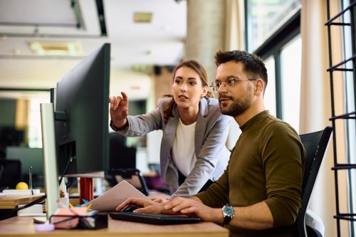 Young entrepreneur and his female coworker using desktop PC while working in the office.