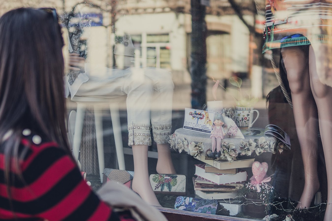 A woman looking at a shop window displaying gifts and clothes.