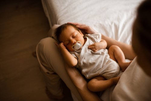 Sleeping baby boy 1-2 months old with pacifier sleeping on mother hands in bedroom closeup top view. Motherhood.