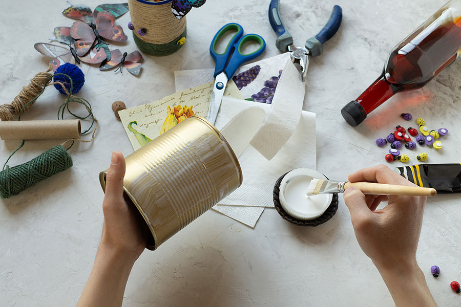 Das Bild zeigt die Hände einer Person, die eine Dose mit Leim bestreicht, um sie dann mit Papier und anderen Materialien zu bekleben – DIY-Ideen für Upcycling-Materialien