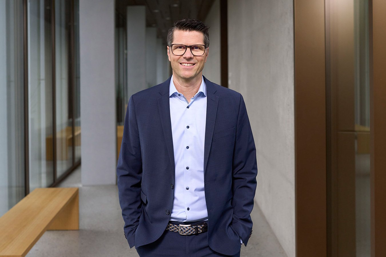 Thomas Jakob, Head of Sustainability at PostFinance and responsible for sustainability, stands in a modern office building with a smile.